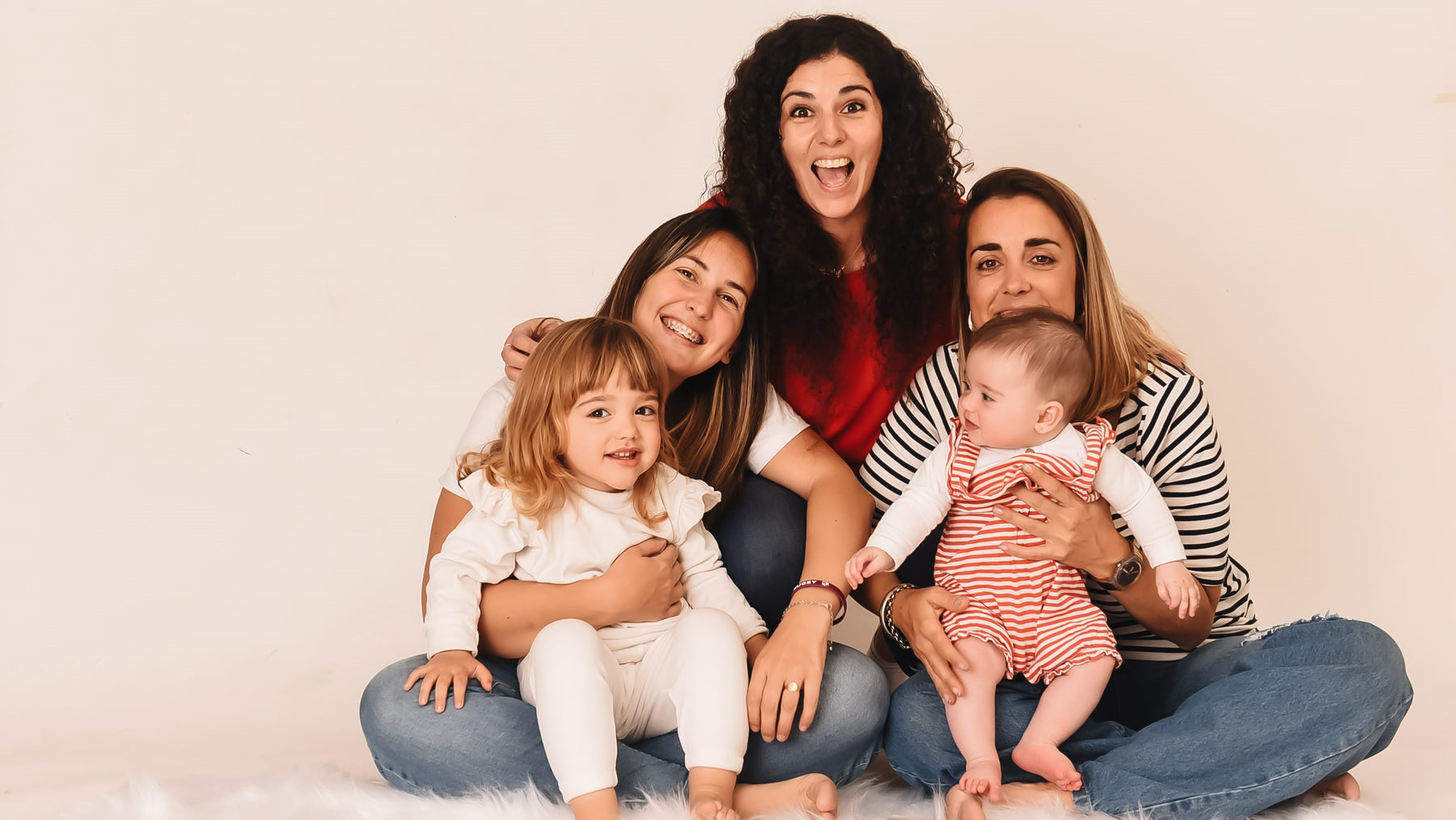 Three women are posing and laughing with two toddlers. Parenting hacks, kids activities, educational fun.