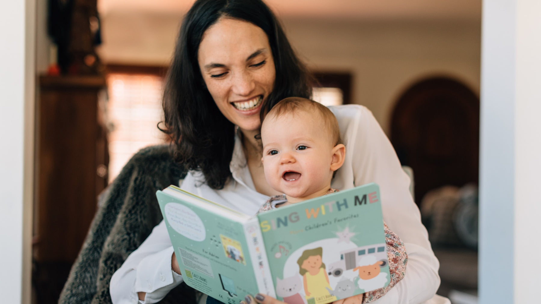 A Mom is singing and reading a book to her baby. Musical books, kids, language, skills.