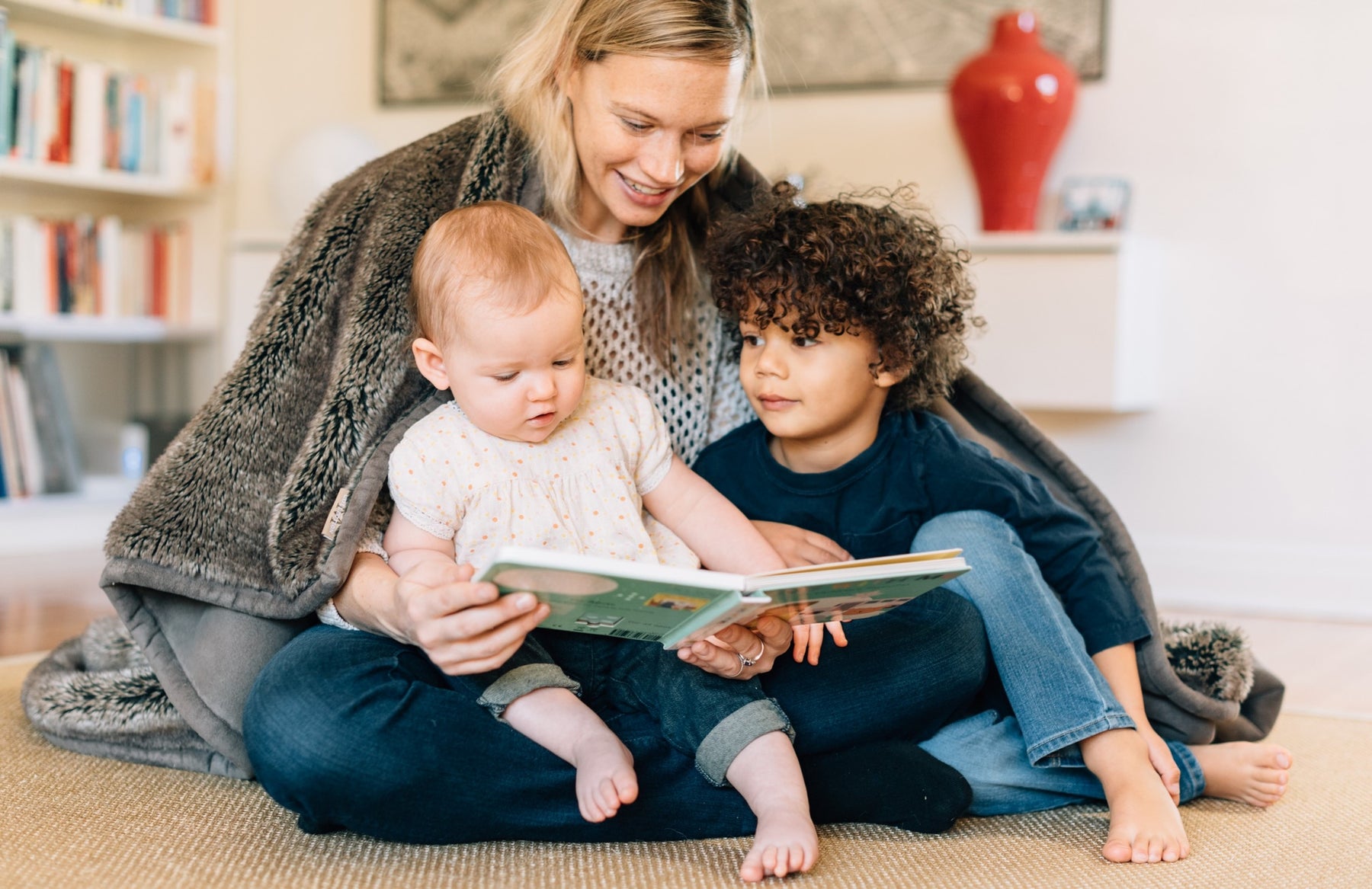 A Mom is reading a book to a toddler girl and little boy. Sound books, musical toys, kids education.
