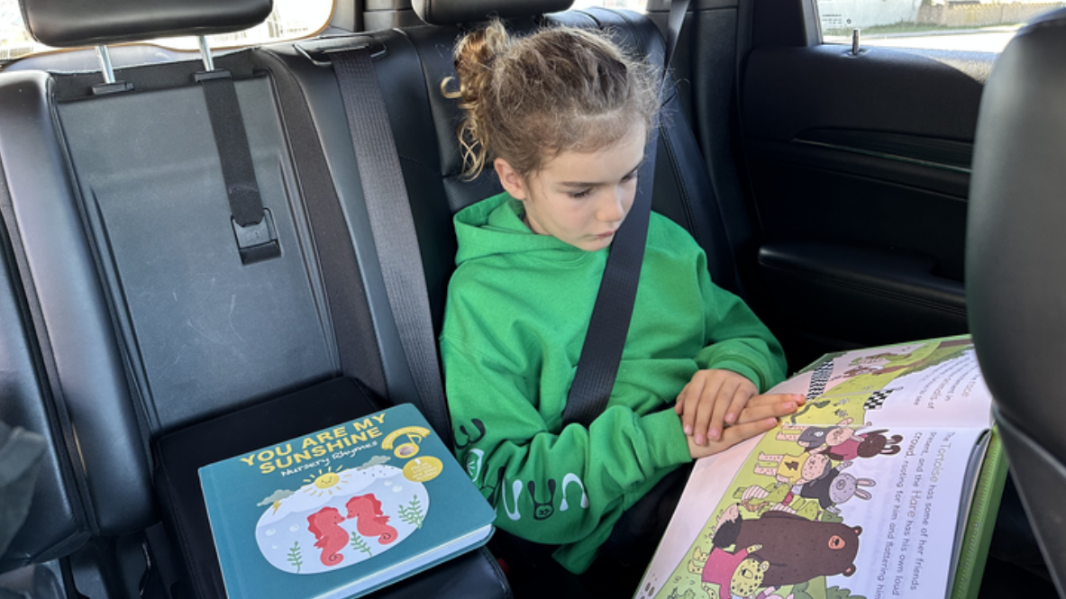 A girl is reading picture books in the car. Kids, fun activities, educational books.
