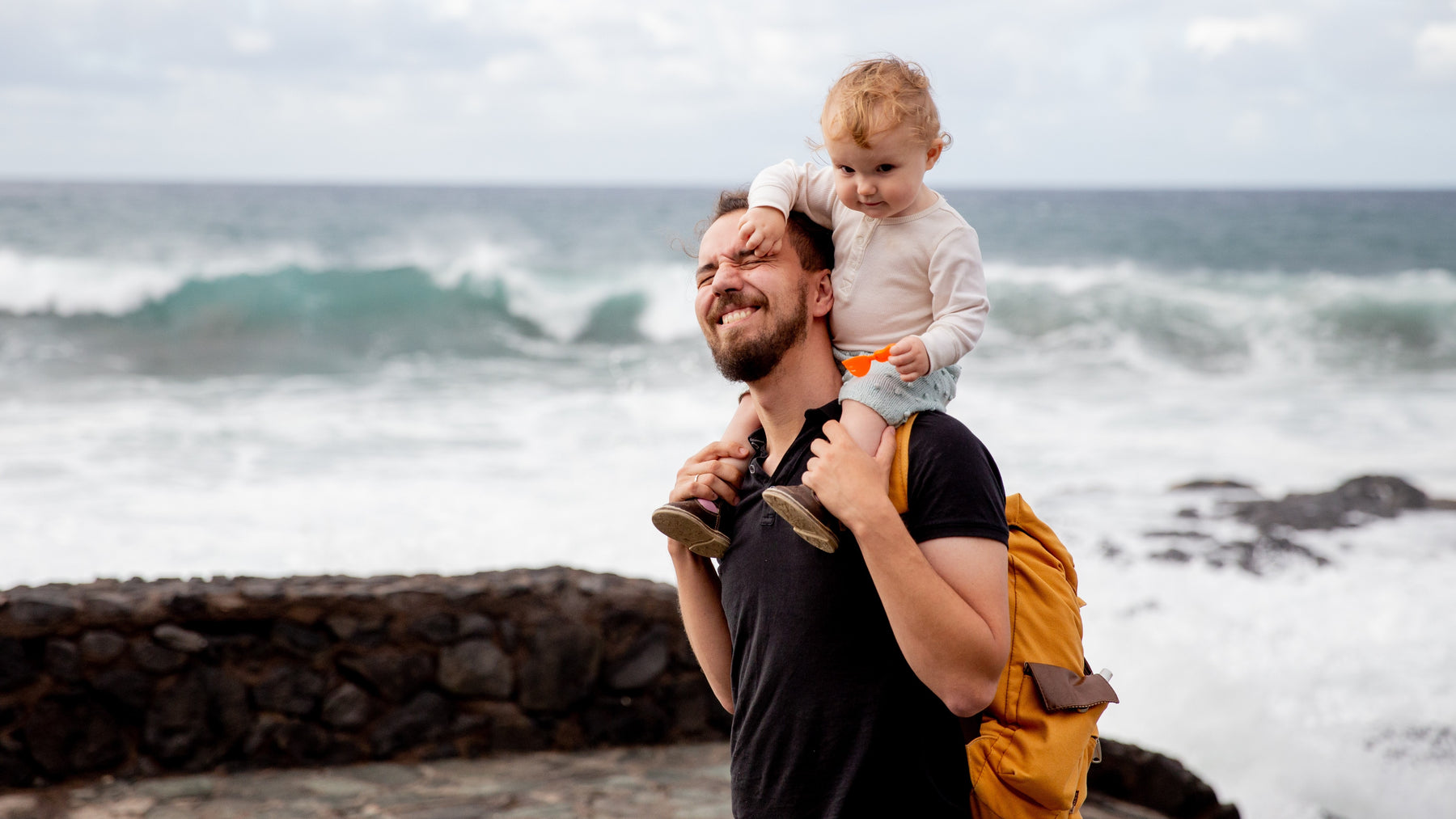 A Dad is holding his toddler son on a trip to the beach. Family, travel tips.