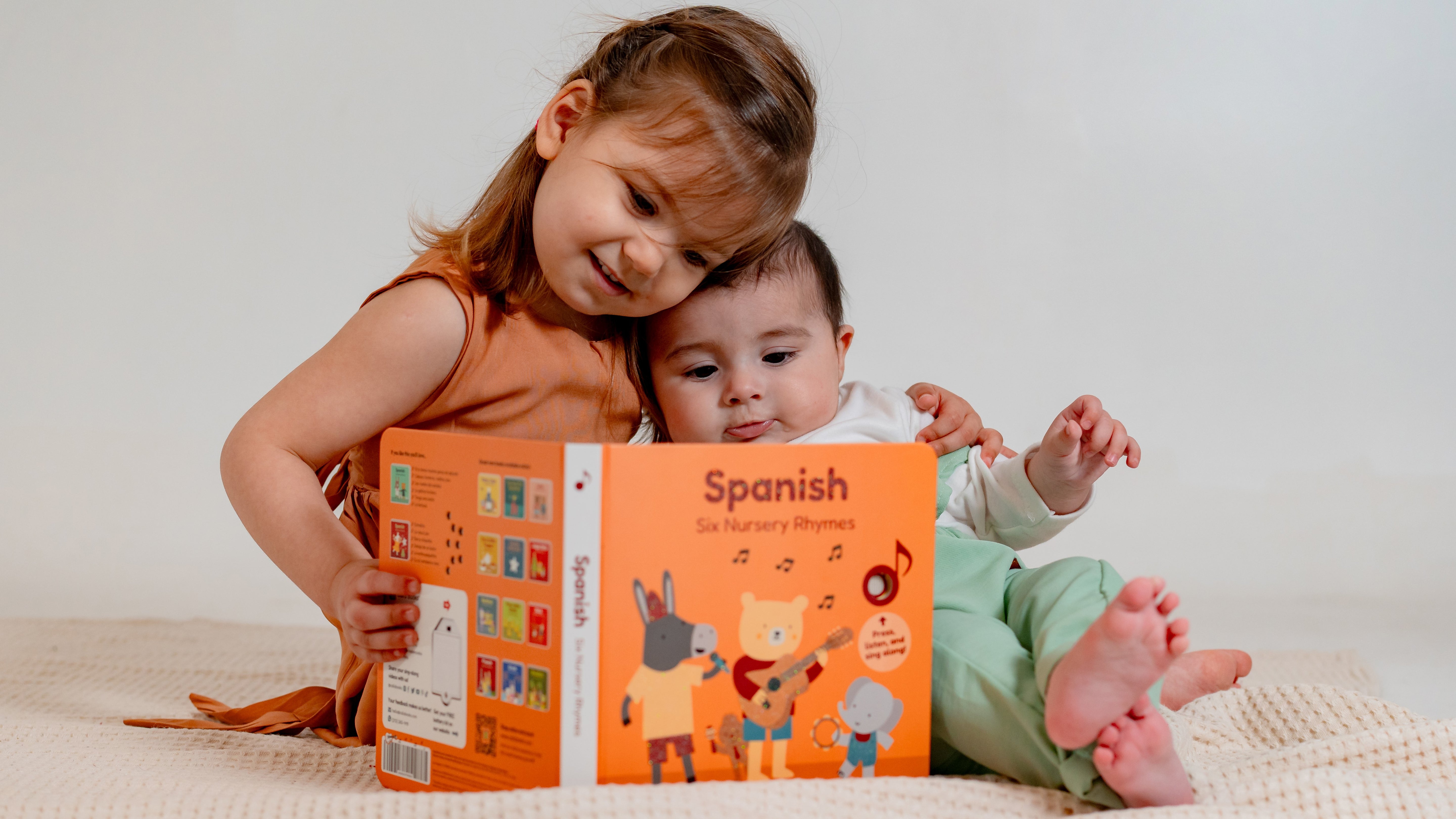 A little girl and a baby are reading a spanish book. Spanish books, bilingual books, children books, kids language, language books for kids.