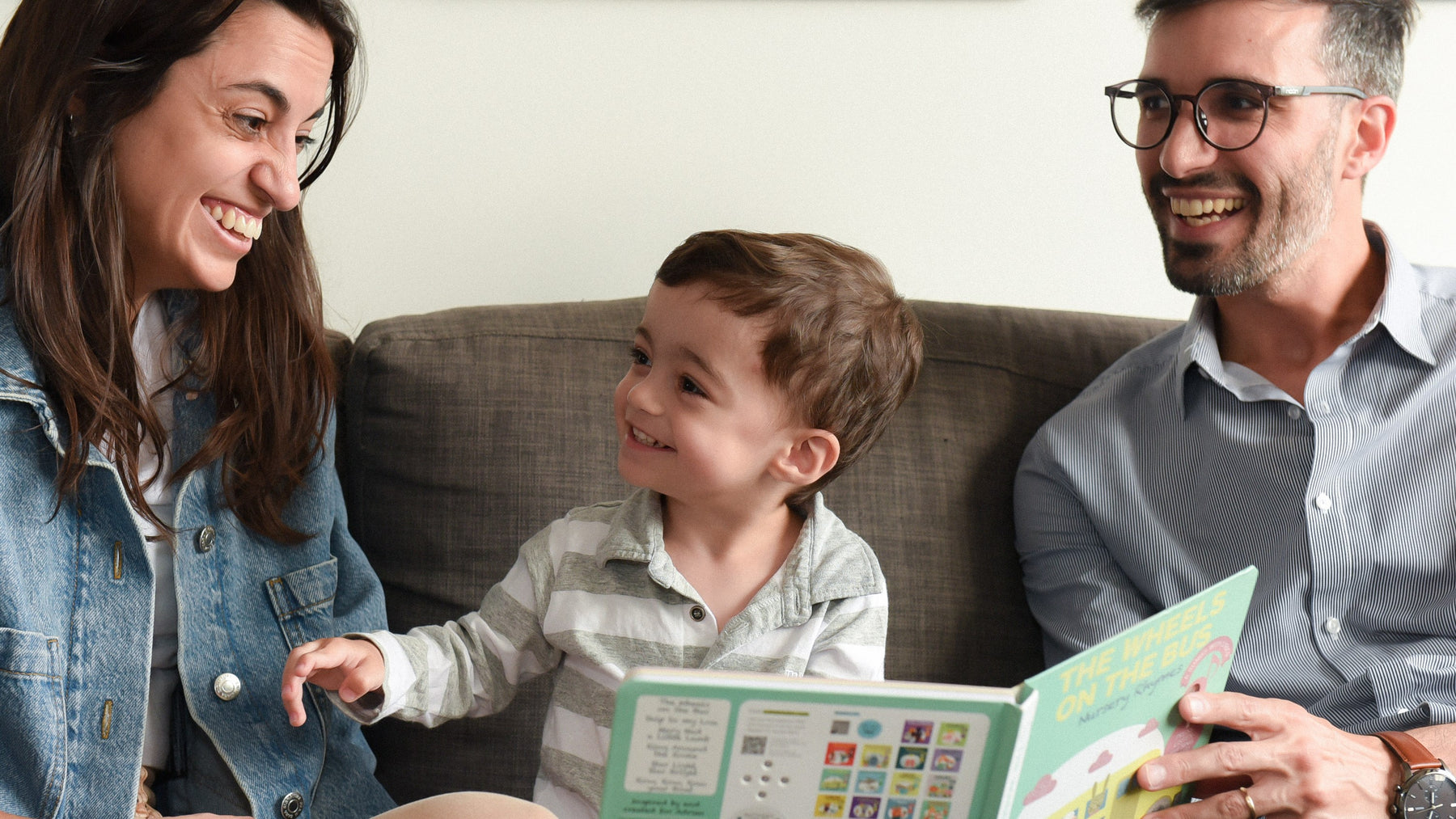 A Mom and a Dad are reading a book to their toddler. Best parenting books, toddler, kids activities, education.