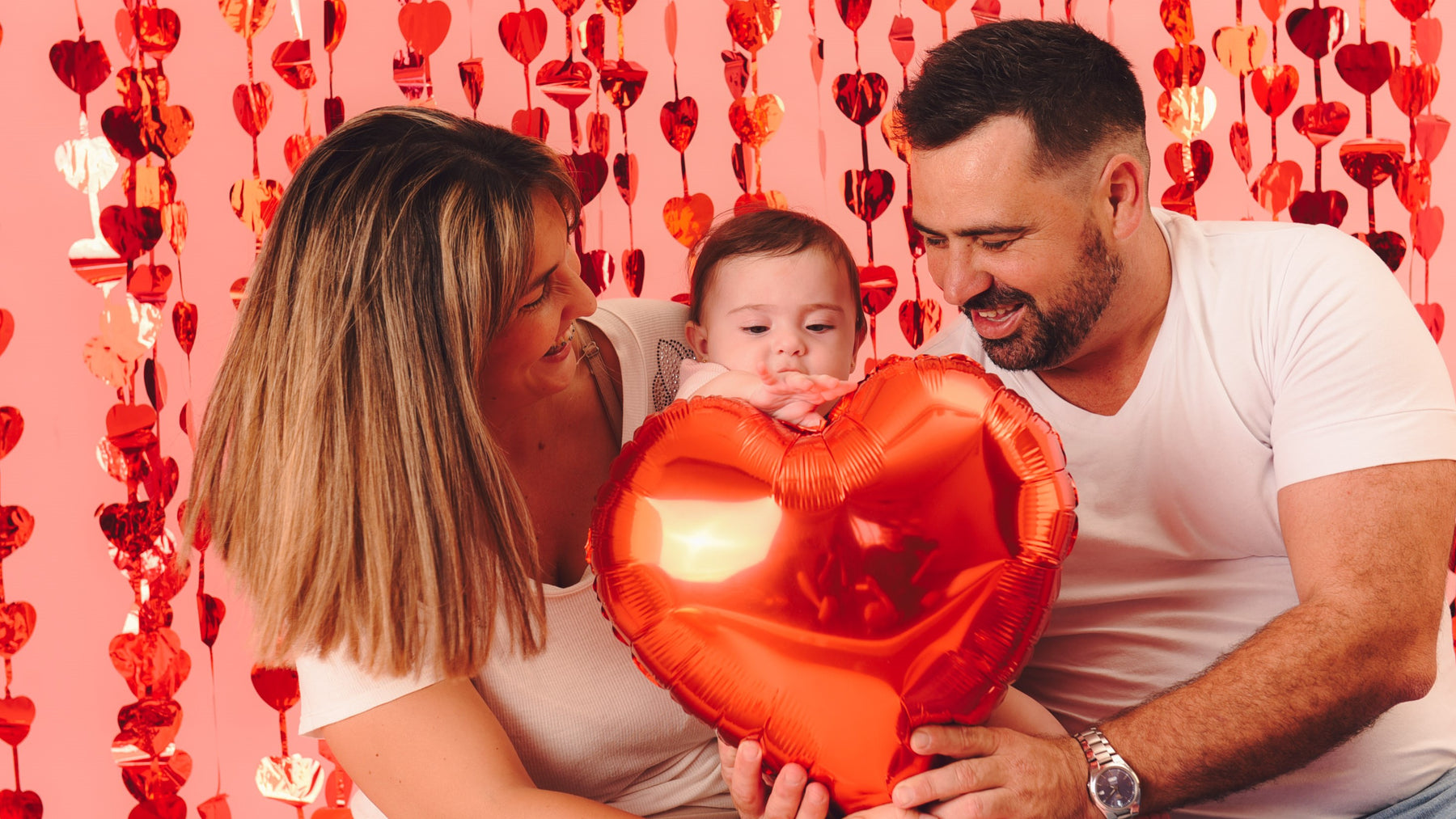 A Mom and a Dad kissing their toddler with a heart shaped balloon. Creative gifts, activities for kids, valentine's day.