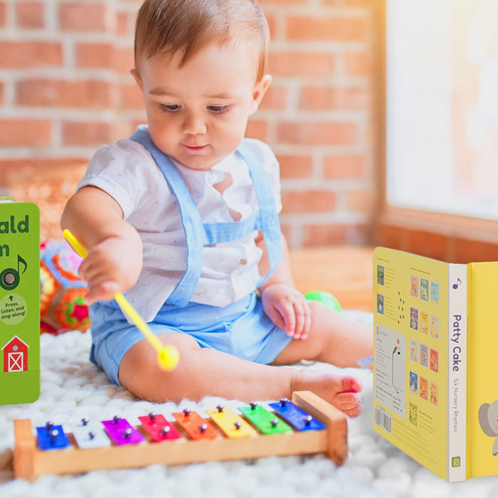 A baby is playing on a keyboard and sitting down on a carpet with musical books. Babies songs, children musical books, educational, music activities.