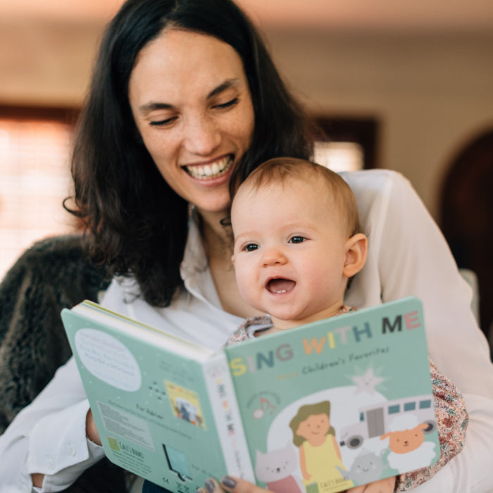 A Mom is singing and reading a book to her baby. Musical books, kids, language, skills.
