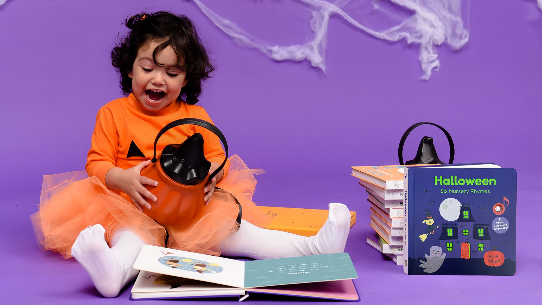 A toddler is playing with a pumpkin next to a pile of Halloween books. Family, fun Halloween activities, kids books.