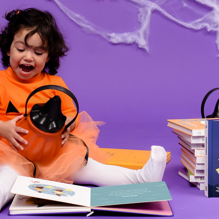 A toddler is playing with a pumpkin next to a pile of Halloween books. Family, fun Halloween activities, kids books.