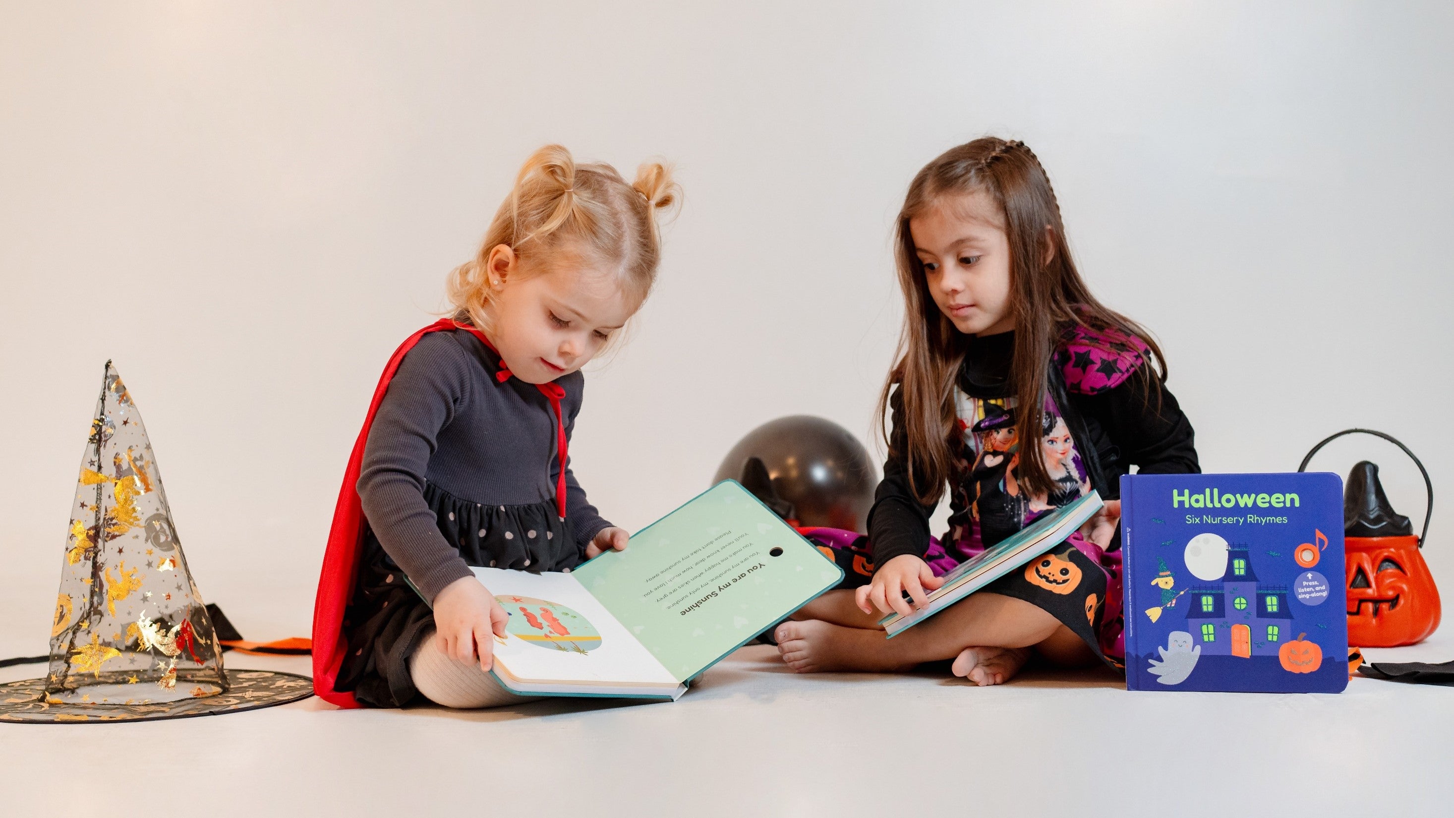 Two girls dressed as witches are sitting down and reading picture books. Halloween books, halloween activities, halloween tips, kids books, kids reading.