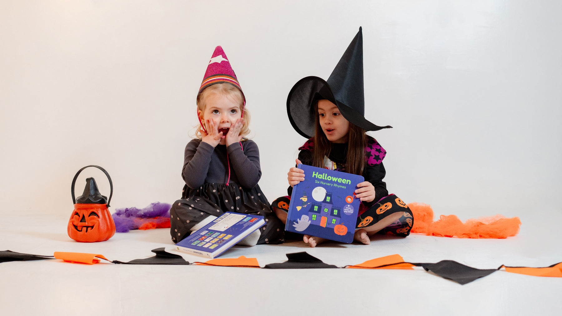 Two young girls are dressed up in halloween costumes sitting down and holding books. Halloween, kids activities, safety tips, fun activities, halloween costumes.
