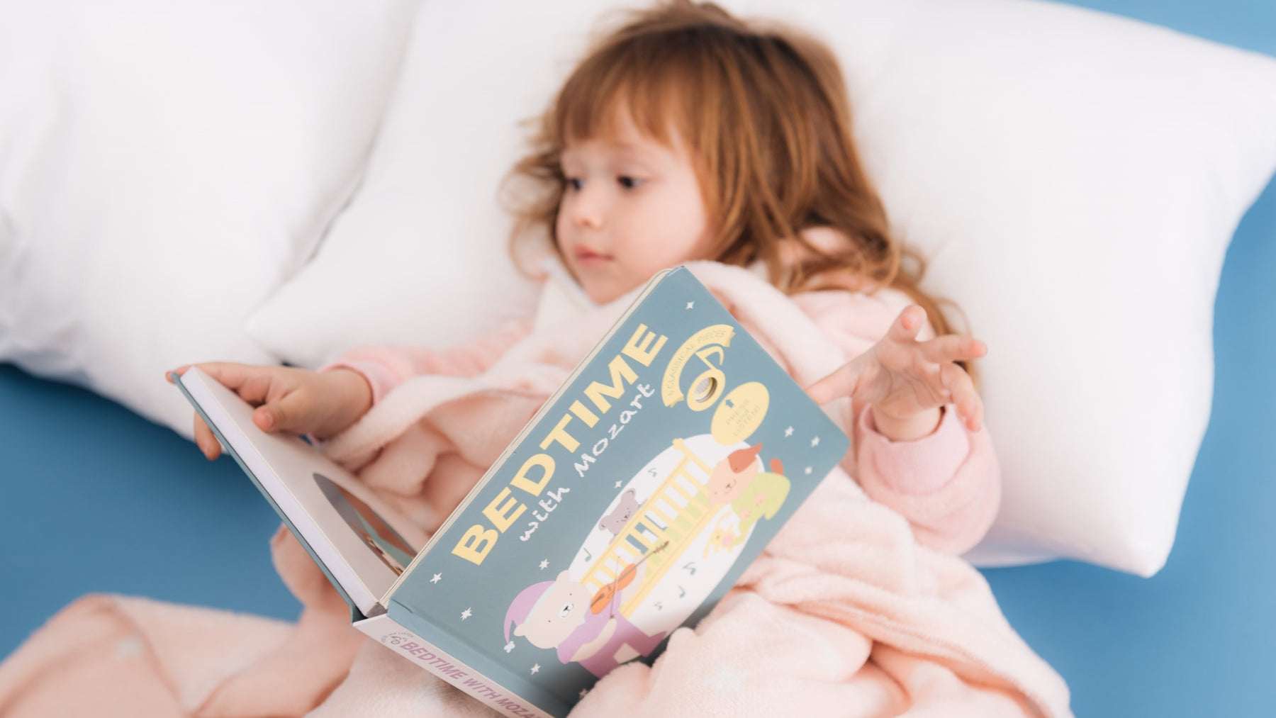 A toddler girl is reading in bed. Bedtime stories, kids activities, educational.