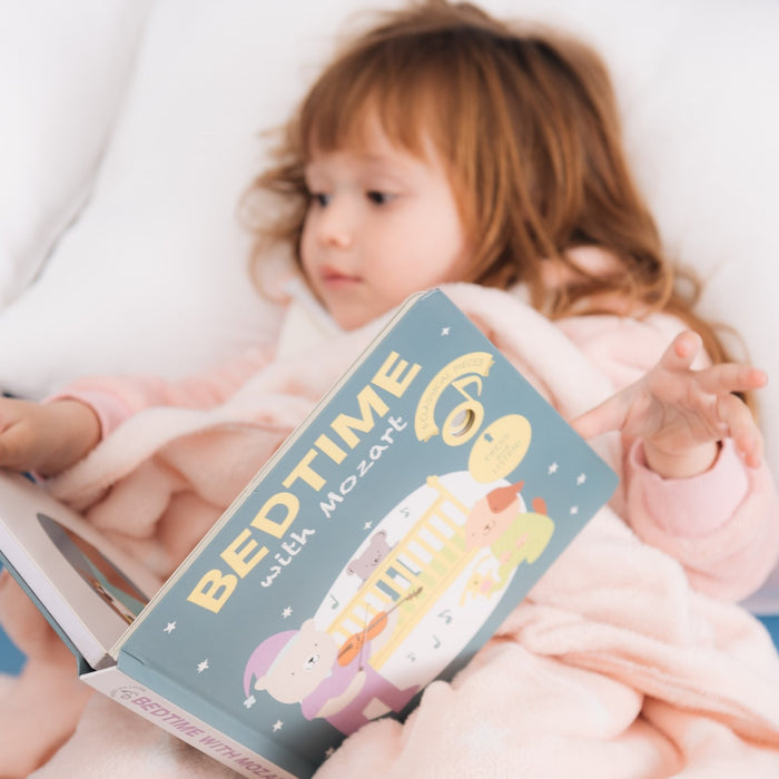 A toddler girl is reading in bed. Bedtime stories, kids activities, educational.