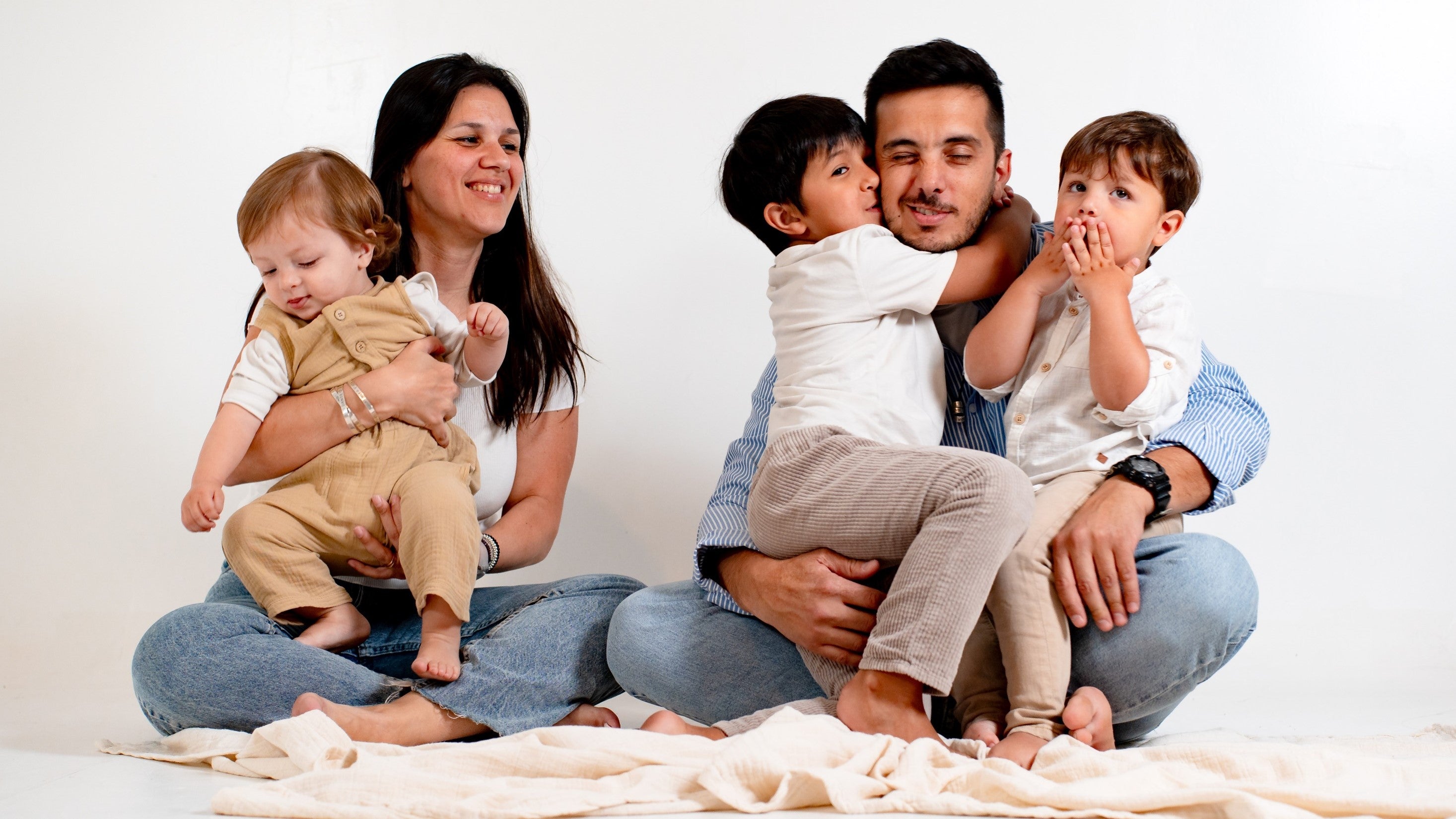 A mom and a dad are hugging their 3 children whilst sitting on the floor. Kids education, parenting goals, new year resolutions.