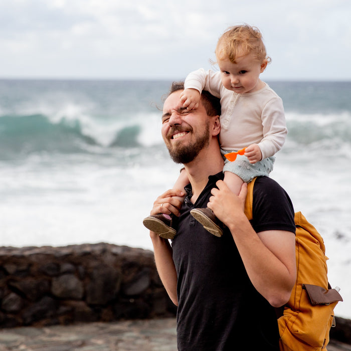 A Dad is holding his toddler son on a trip to the beach. Family, travel tips.