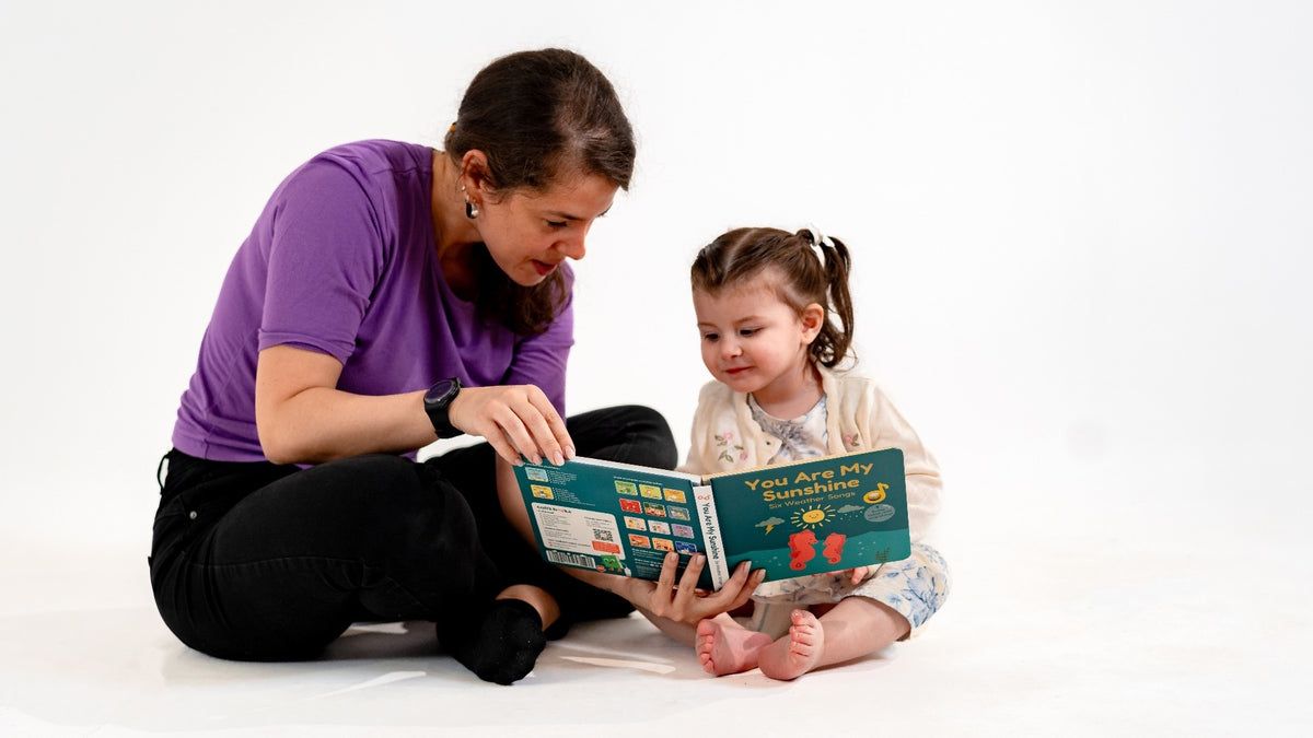 A mom is reading a picture book to her toddler girl. You are my sunshine, musical books, kids songs, kids activities.